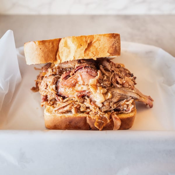 A close-up of a pulled pork sandwich on white bread, served in a paper-lined basket.