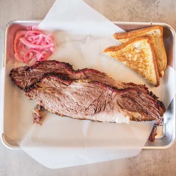 Smoked brisket with pickled red onions and toasted bread on a metal tray.