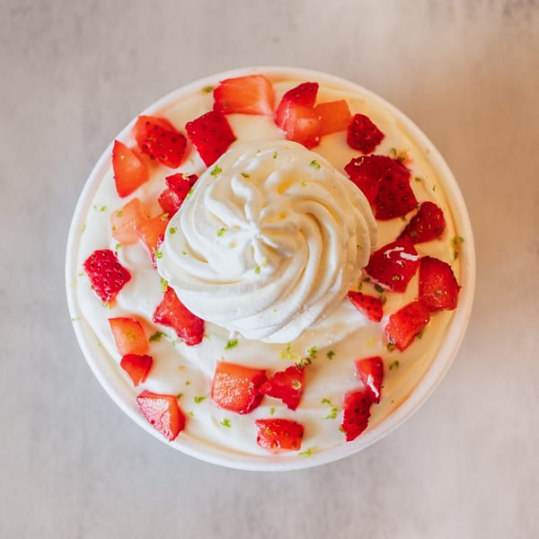 Overhead view of a dessert cup with whipped cream, diced strawberries, and lime zest.