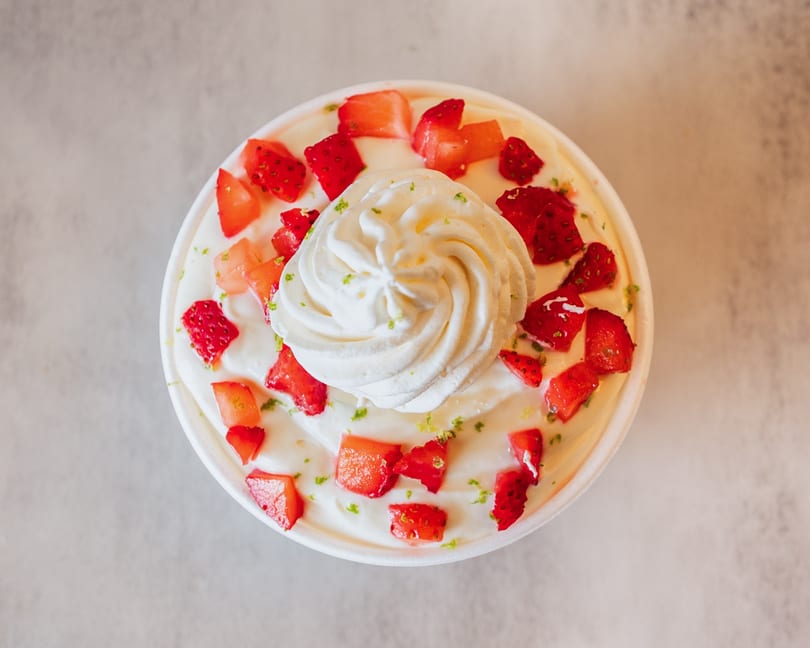 Overhead view of a dessert cup with whipped cream, diced strawberries, and lime zest.