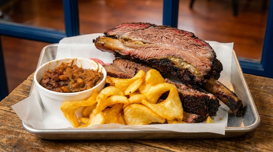 Smoked beef ribs, steak fries, and baked beans served on a metal tray with parchment paper.