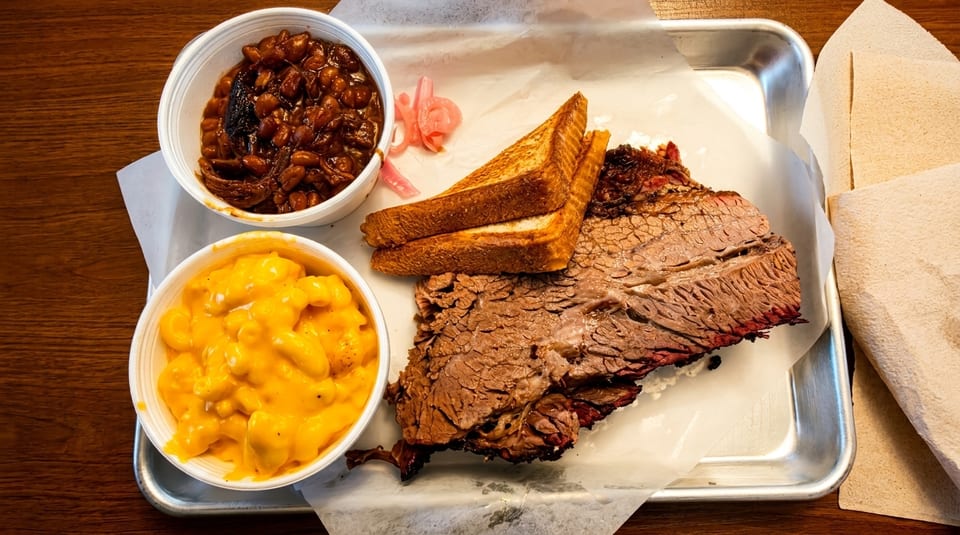 Barbecue brisket plate with mac and cheese, baked beans, toast, and pickled onions on a metal tray.
