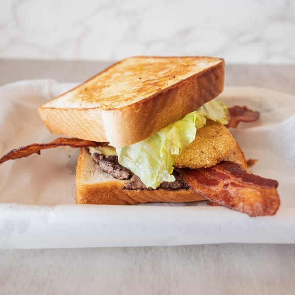 A toasted sandwich with bacon, lettuce, a fried green tomato, and a burger patty.
