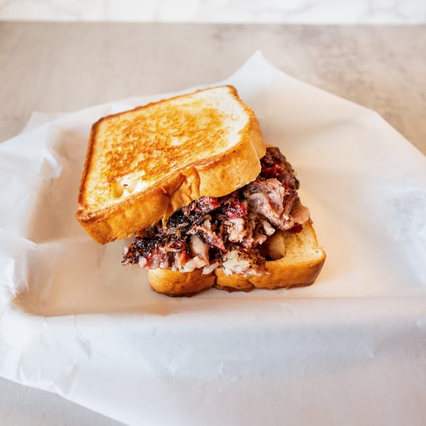 A grilled sandwich with toasted bread and a generous filling of dark, shredded meat on white paper.