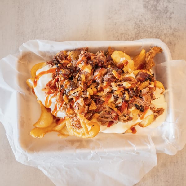 Loaded fries with pulled pork, white sauce, crispy onions, and BBQ drizzle in a paper-lined basket.