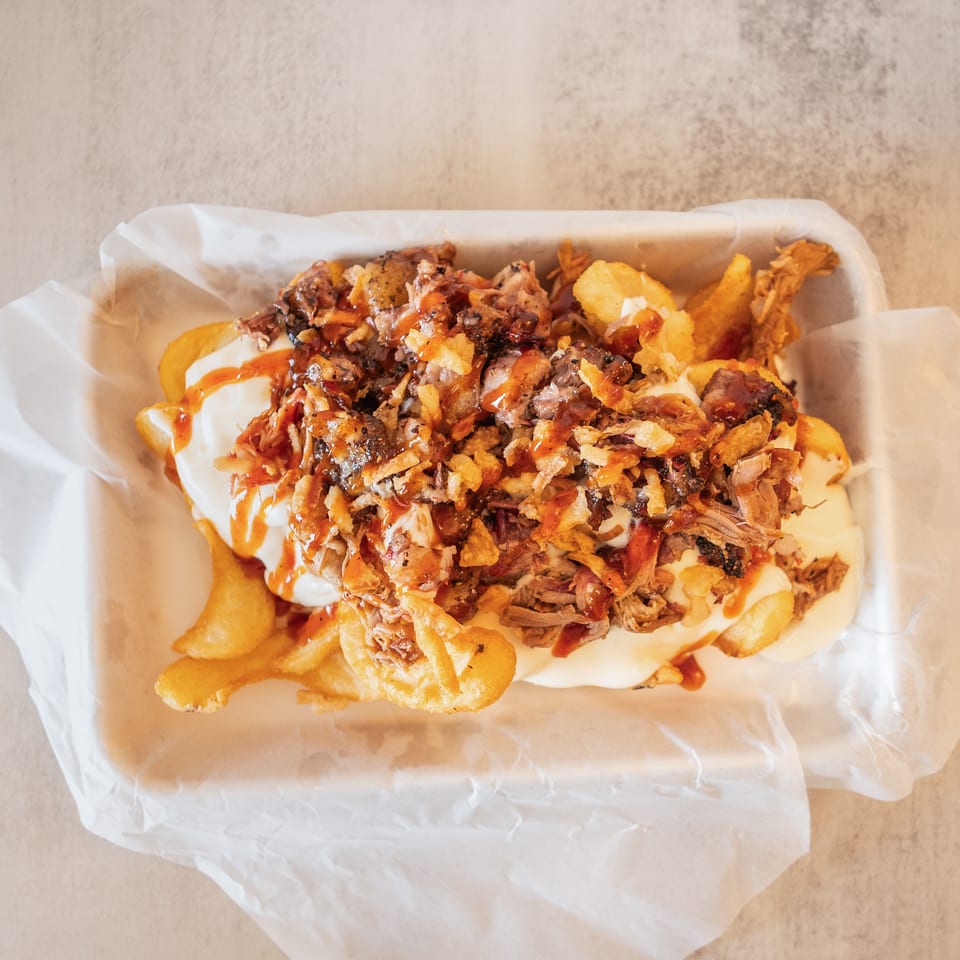 Loaded fries with pulled pork, white sauce, crispy onions, and BBQ drizzle in a paper-lined basket.