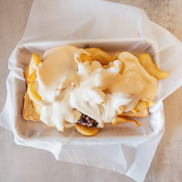 Top-down view of a burger patty and fries on toast, smothered in white cheese sauce.