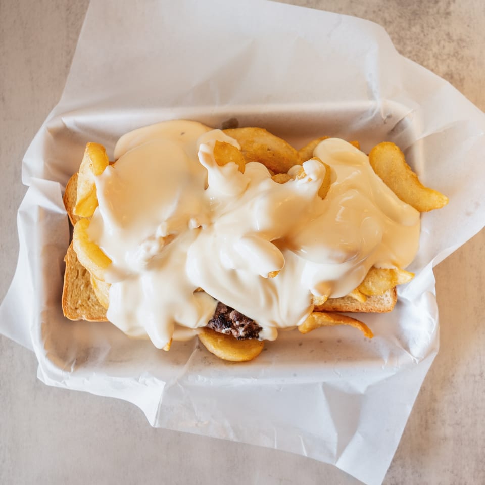 Top-down view of a burger patty and fries on toast, smothered in white cheese sauce.