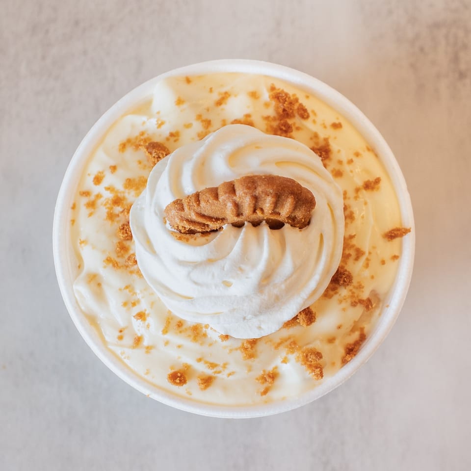 Overhead view of banana pudding with whipped cream and a cookie in a white cup.