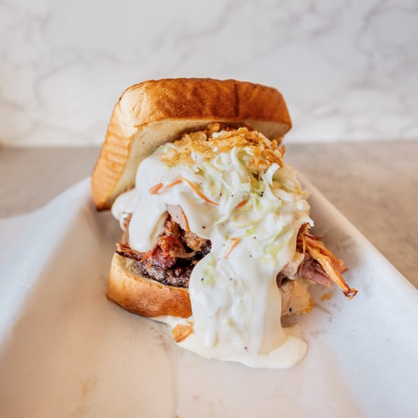 A large sandwich with pulled pork, coleslaw, and creamy sauce on toasted bread.