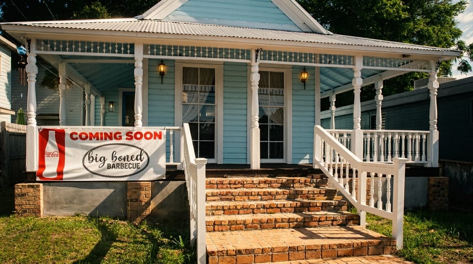 Light blue house with a white porch and brick steps, with a "Big Boned Barbecue Coming Soon" banner.