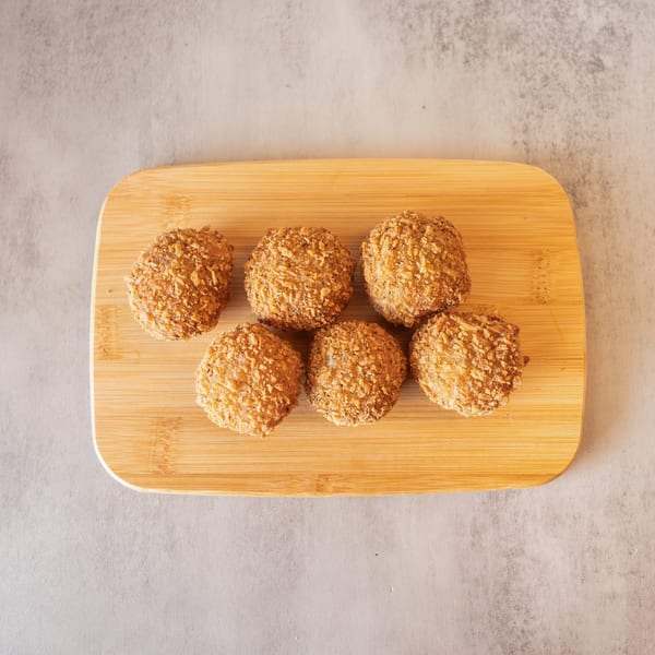 Six golden-brown, breaded croquettes arranged on a light wooden cutting board.