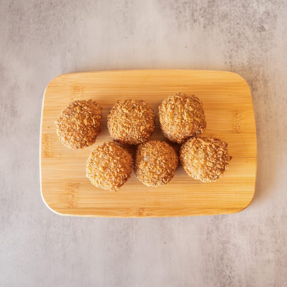 Six golden-brown, breaded croquettes arranged on a light wooden cutting board.