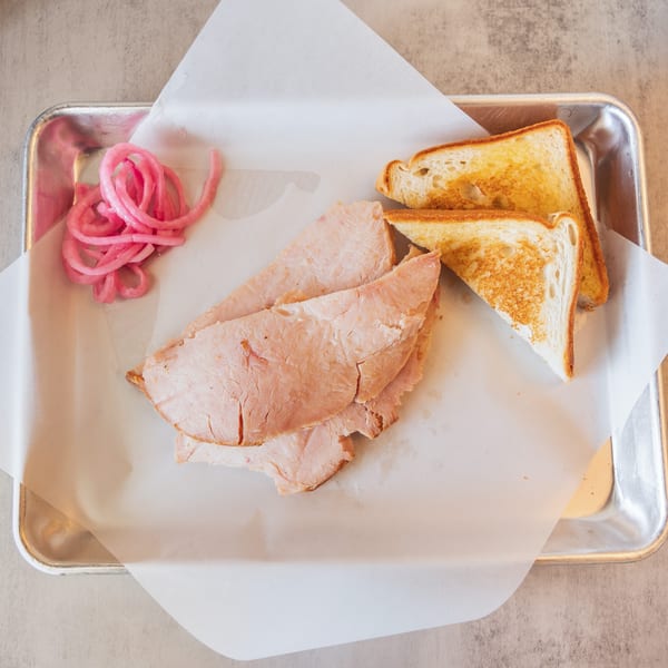 Sliced turkey, toasted bread, and pickled red onions on a metal tray with parchment paper.