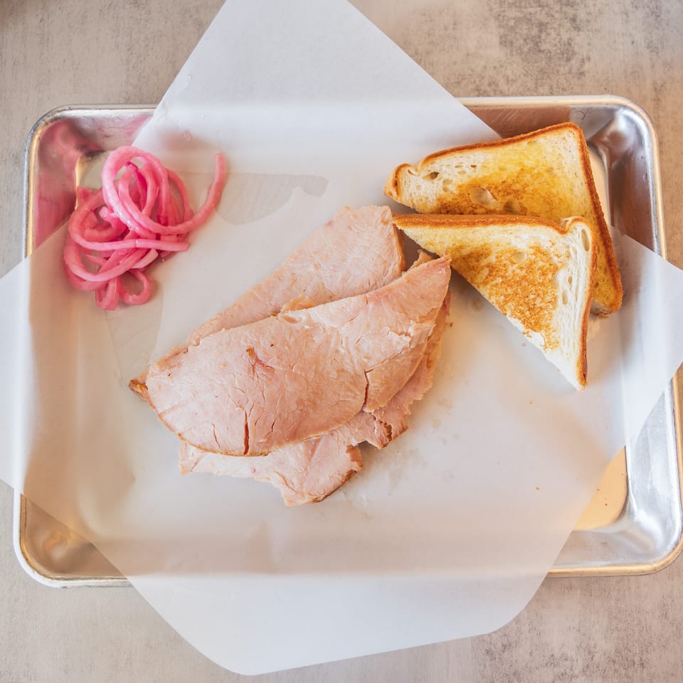 Sliced turkey, toasted bread, and pickled red onions on a metal tray with parchment paper.