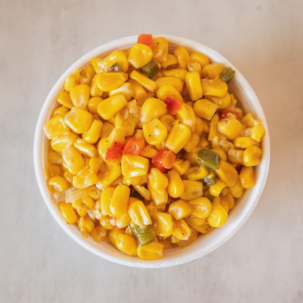 Overhead view of a white bowl filled with yellow corn, red, and green bell peppers.