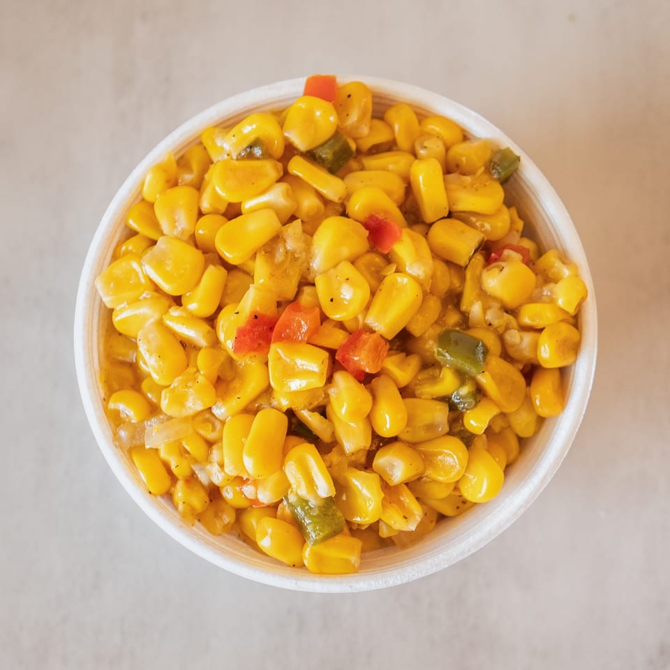 Overhead view of a white bowl filled with yellow corn, red, and green bell peppers.