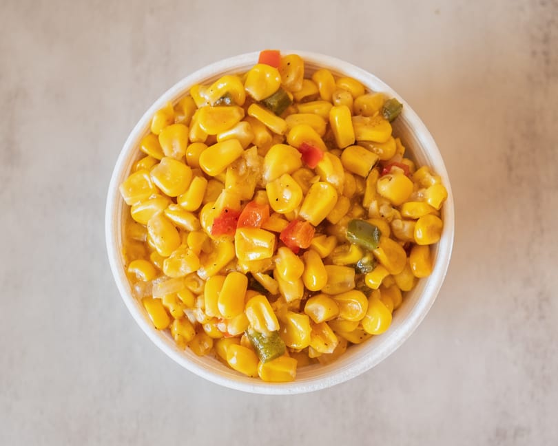 Overhead view of a white bowl filled with yellow corn, red, and green bell peppers.